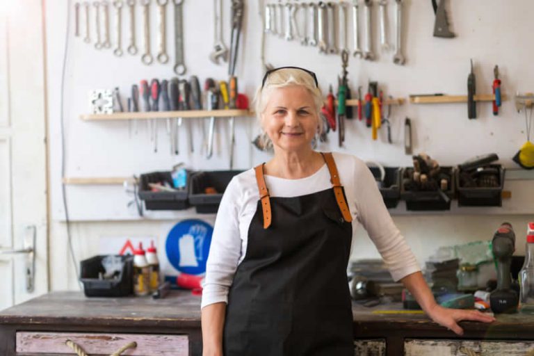 Senior woman entrepreneur in workshop apron smiling in organized craft studio - Manitoba small business owner