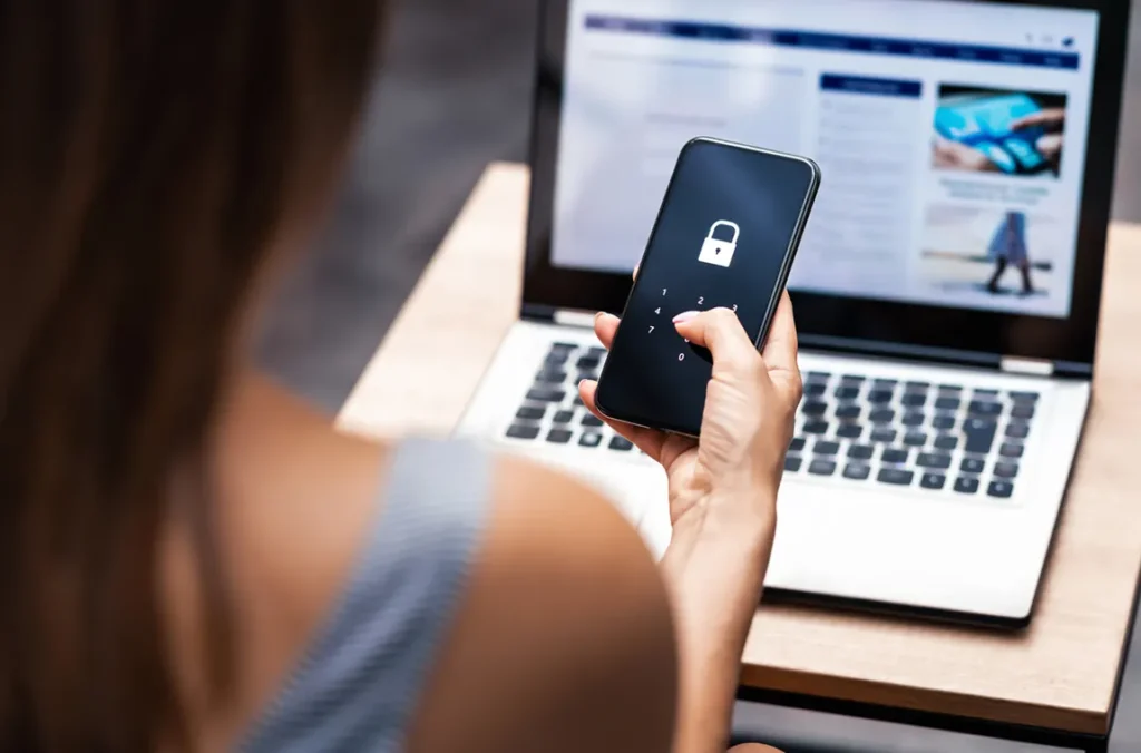 Person holding smartphone with lock icon and security keypad while using laptop for Ontario company key registration and business security verification