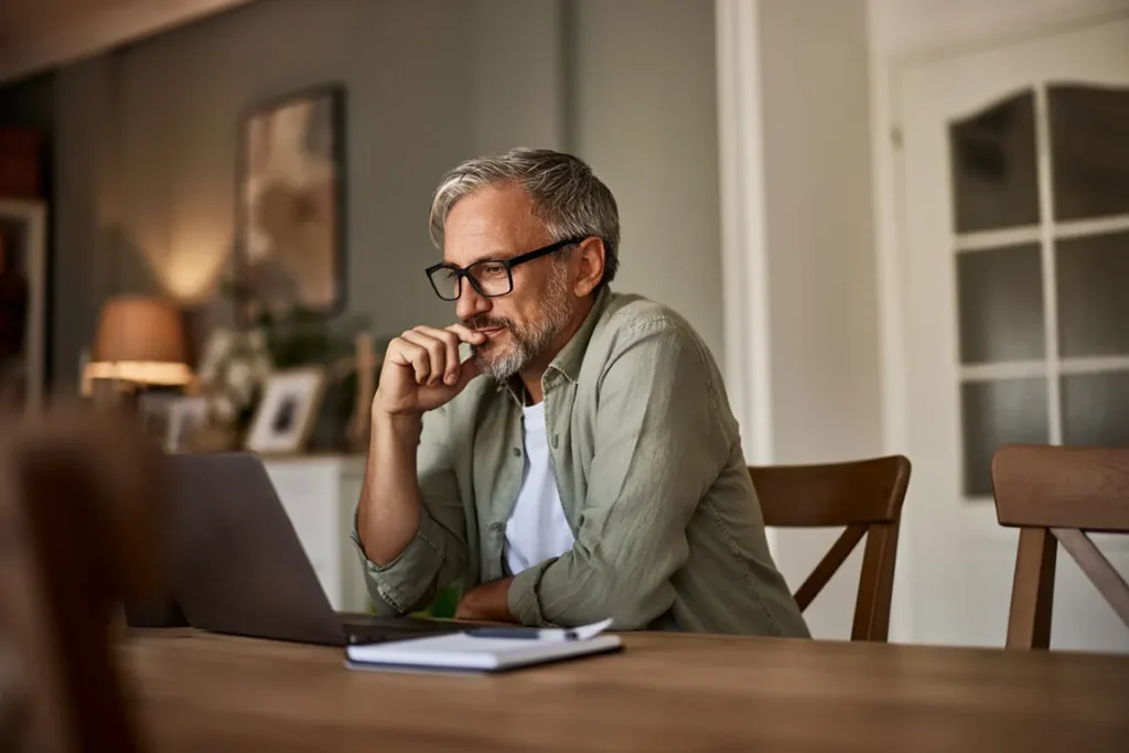 Professional man conducting PPSA search online at home office desk with laptop and documents