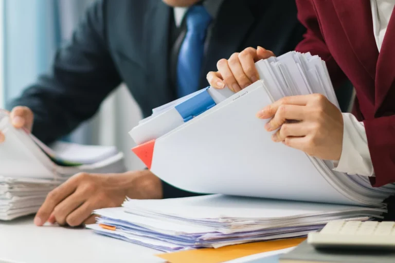 Two business professionals search through paperwork at a desk, focused on locating their corporation number.