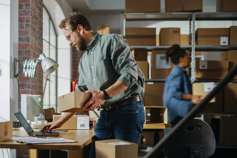 Entrepreneur multitasking with computer and packages in fulfillment center while operating multiple business ventures