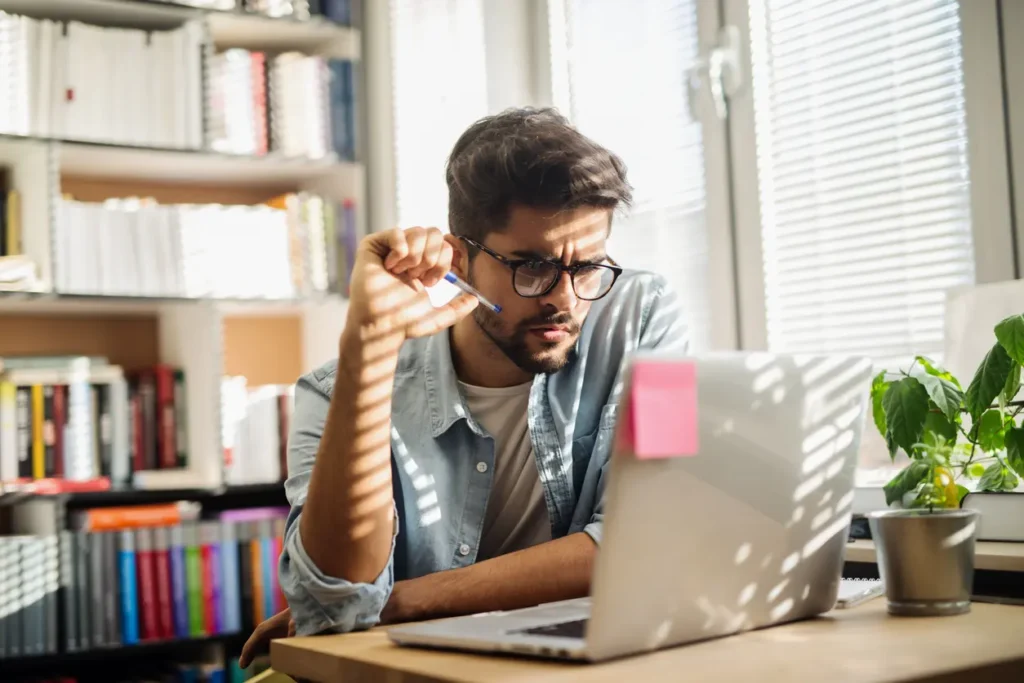 Business owner researching incorporation documents on laptop in modern home office with bookshelves and natural lighting
