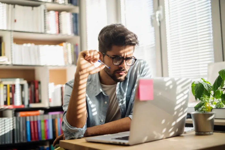 Business owner researching incorporation documents on laptop in modern home office with bookshelves and natural lighting