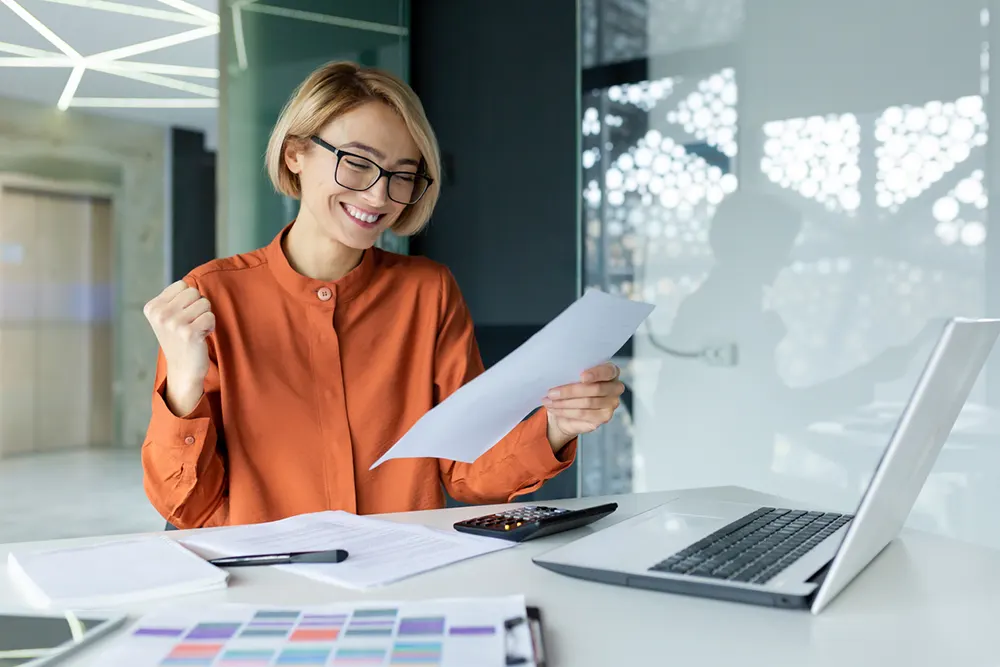 Happy business owner reviewing HST documents at desk with laptop - Ontario sales tax management guide