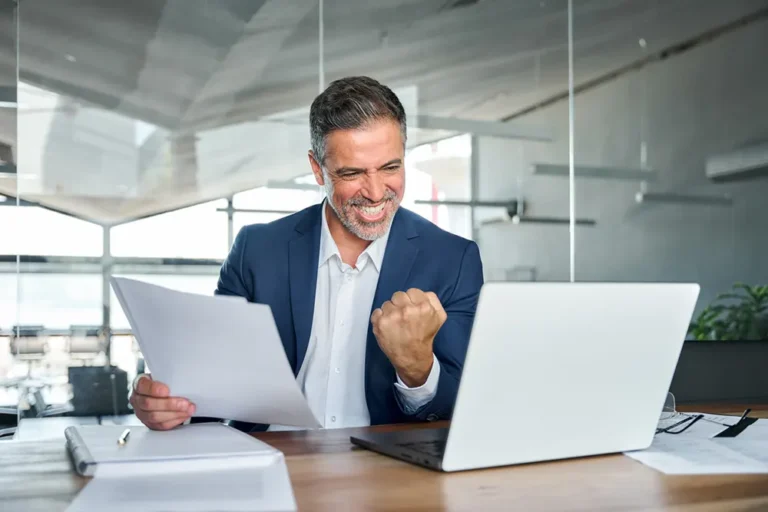 Entrepreneur in modern office fist‑pumping at laptop upon receiving instant NUANS report