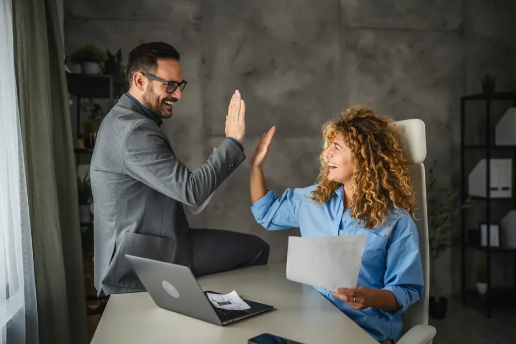 Business professionals celebrating successful Ontario business registration renewal with high-five in modern office