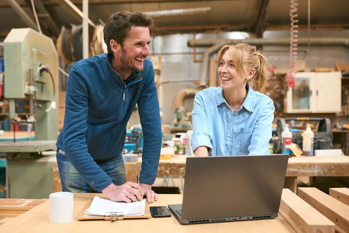 Two small business owners smiling in a woodworking shop while planning and registering their Ontario business.