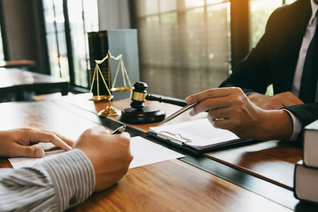 Corporate law meeting: client and attorney review and sign incorporation papers beside gavel and scales.