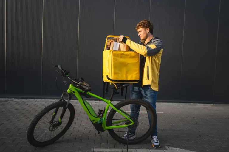 Young man with a bicycle and yellow delivery bag organizing food orders, representing flexible side hustle jobs like bike courier or food delivery service.