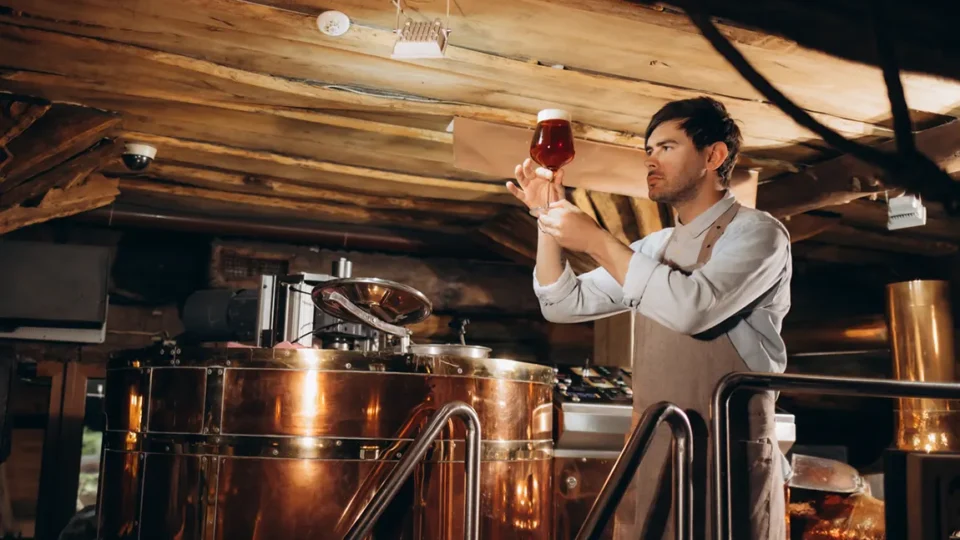 Craft brewer inspecting beer quality at copper brewing equipment in Ontario microbrewery requiring liquor license