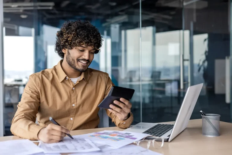 Canadian side hustler reviewing tax documents and using mobile phone at desk with laptop for income tracking and tax preparation