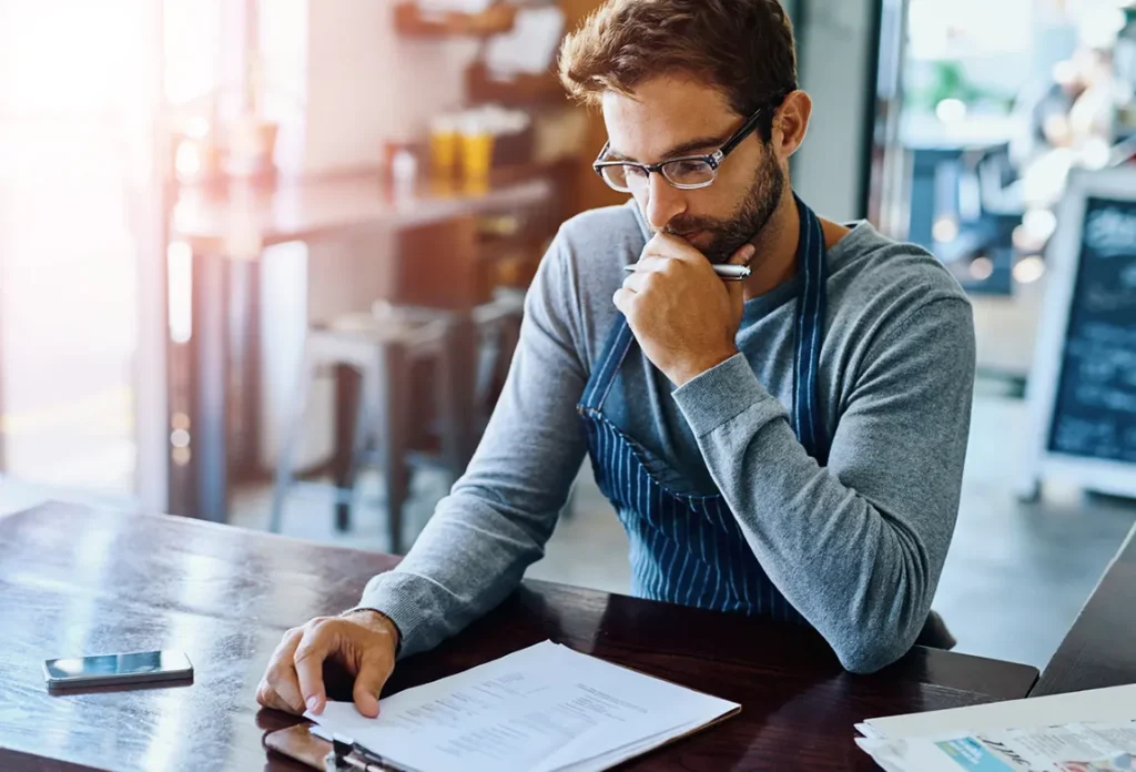 Small business owner carefully reviewing incorporation paperwork and legal documents at cafe