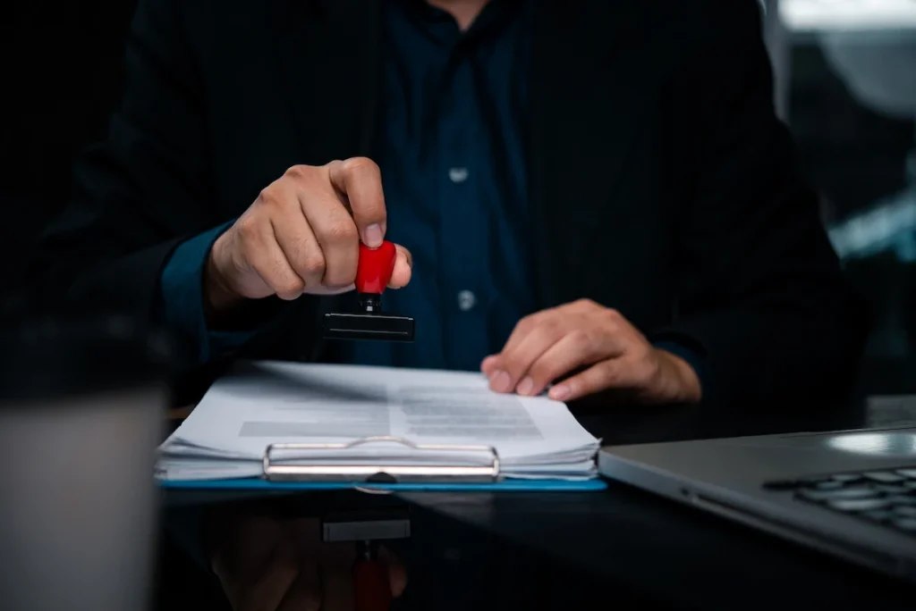 A professional in a suit holds a red rubber stamp, ready to approve a trademark application.