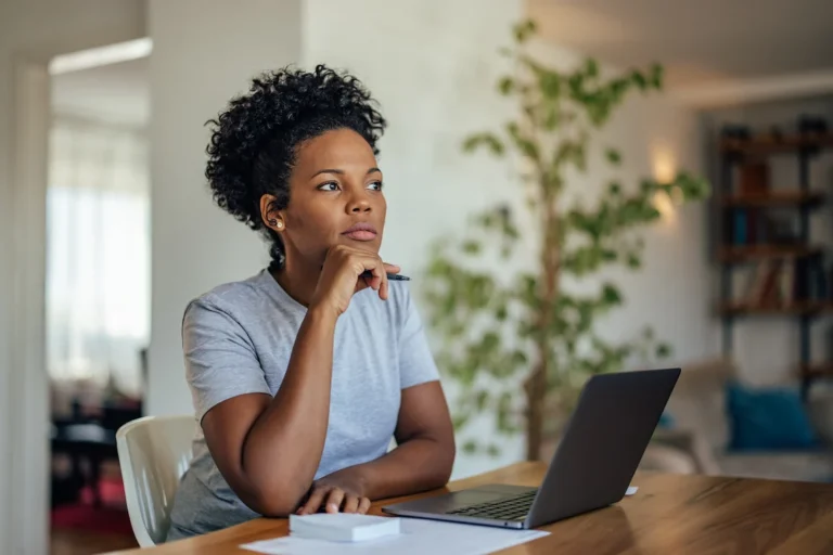 A woman working on a laptop at a table, engaged and thoughtful researching a company's legal status.