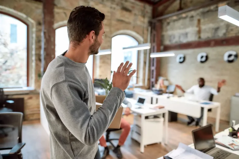A man waves goodbye to colleagues in an office, marking his departure to start his own business venture.