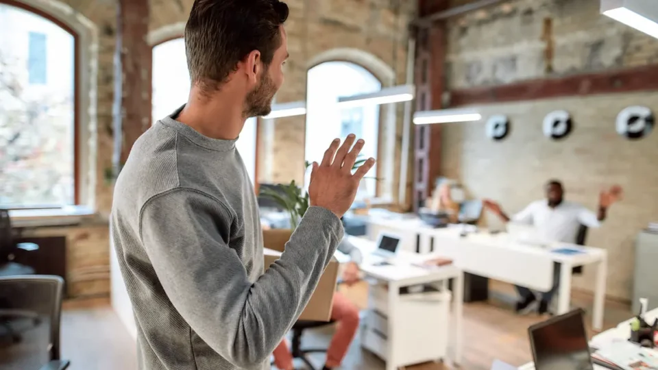 A man waves goodbye to colleagues in an office, marking his departure to start his own business venture.