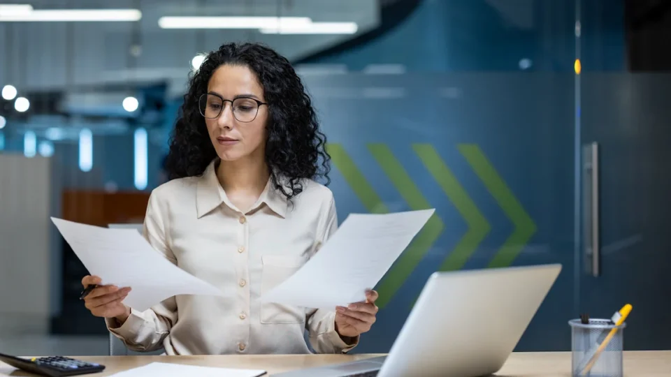 A woman examines documents at her desk, comparing a business registration with a business license.