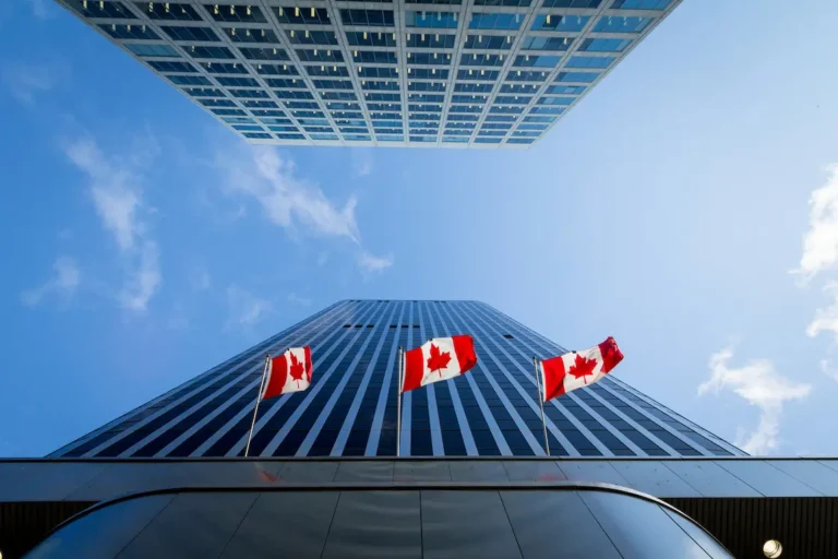 Canadian flags wave in front of a tall building against a clear blue sky.