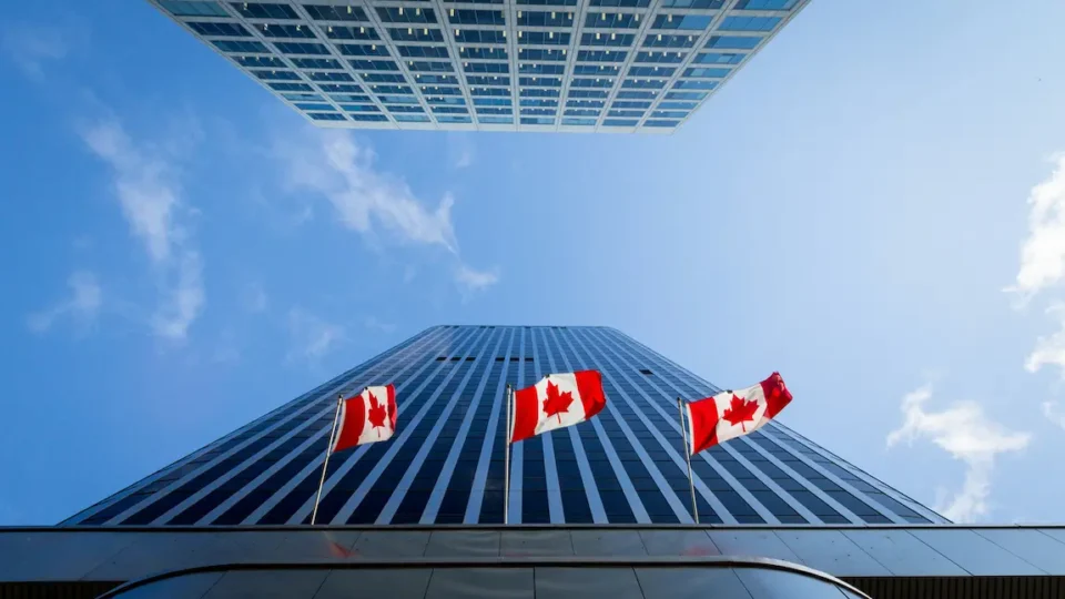 Canadian flags wave in front of a tall building against a clear blue sky.