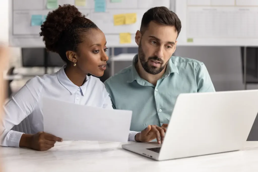 A man and woman examining a laptop, comparing corporate names, trade names, and trademarks in a collaborative setting.