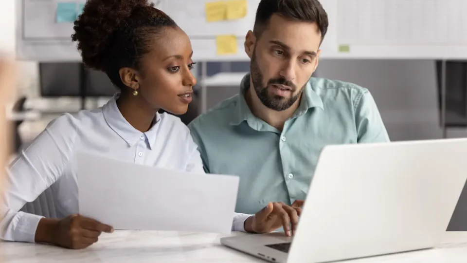 A man and woman examining a laptop, comparing corporate names, trade names, and trademarks in a collaborative setting.