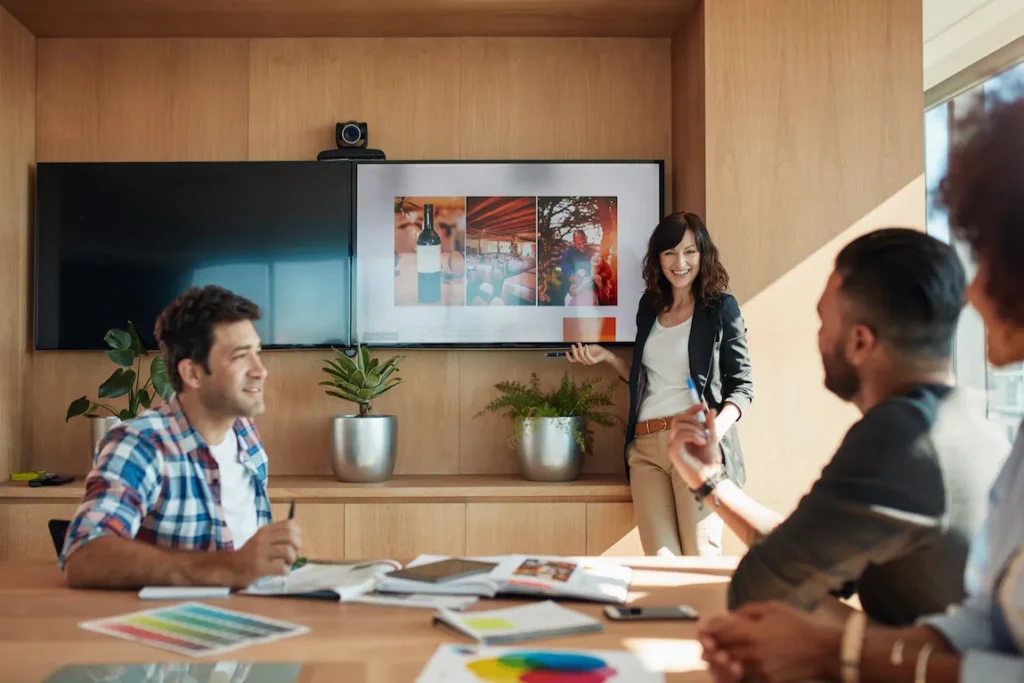 A woman leads a brainstorming session in a meeting room, surrounded by colleagues discussing branding and business names.
