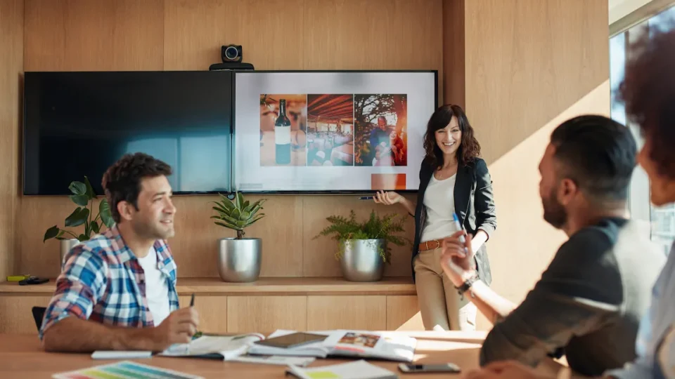 A woman leads a brainstorming session in a meeting room, surrounded by colleagues discussing branding and business names.